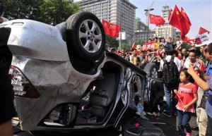 Demonstrators hold Chinese flags and banners beside an overturned car of a Japanese brand during a protest in Xi'an