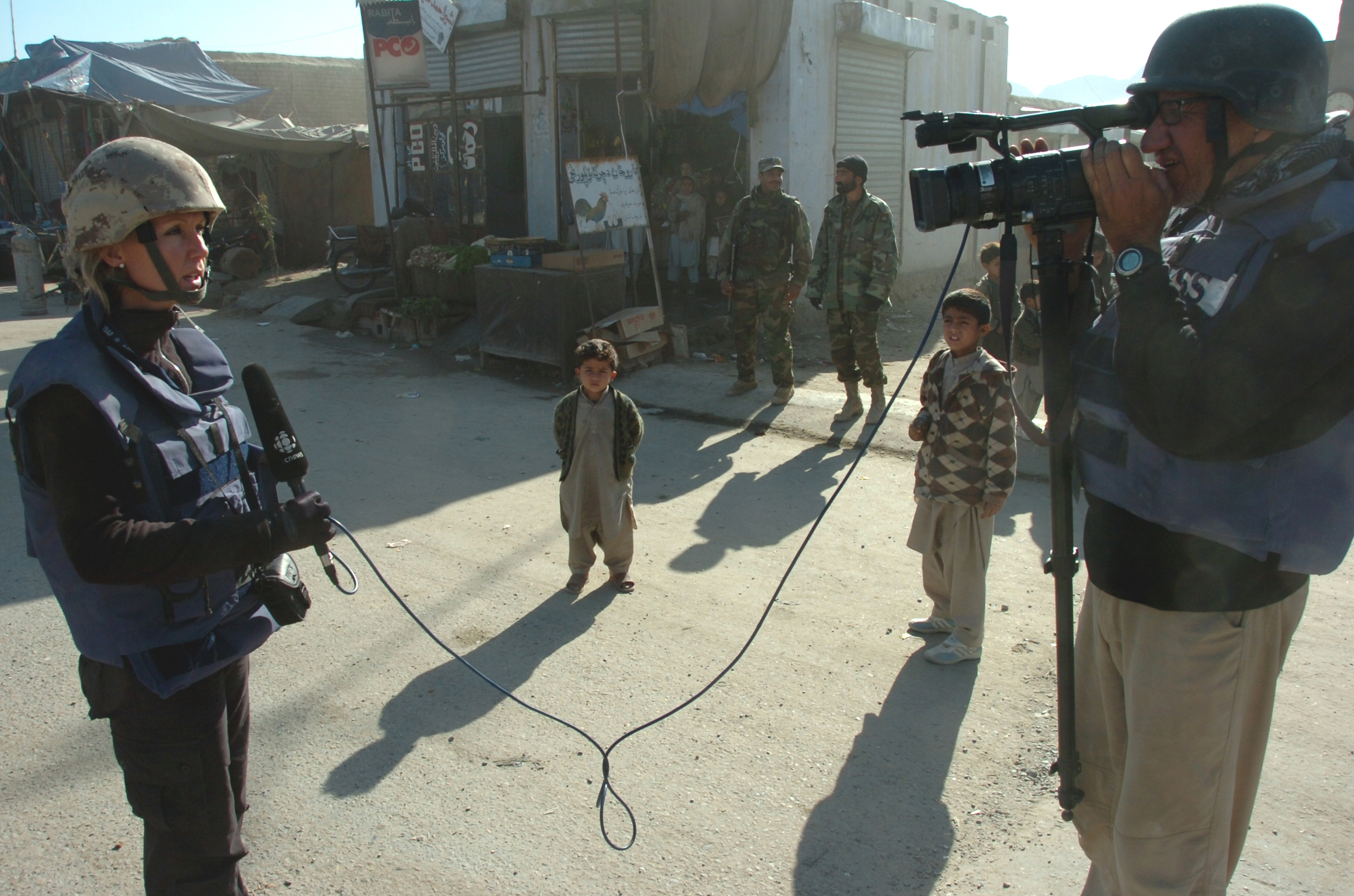 English/Anglais AR2006-S002-0048 December 19, 2006  Kandahar, Afghanistan Reporter Laurie Graham and Cameraman Al Lawrence of the Canadian Broadcasting Corporation (CBC) do an 'on camera' on the main street of Bazaar-e-Panjwaii while two local boys watch with fascination.  CBC joined a Civilian Military Cooperation (CIMIC) Patrol through the streets of Bazaar-e-Panjwaii.  The patrol originated at the gates of Forward Operating Base Ma’Sum Ghar and ended two kilometers east at an Afghan National Army Checkpoint.  Its purpose was to gauge the mood of the town and to do quick assessments of the population.  Joint Task Force Afghanistan (JTF-Afg) is Canada’s contribution to NATO’s International Security Assistance Force (ISAF) in Afghanistan. The focus of this mission is to help Afghans rebuild their lives, families, communities and nation.  Canadian Forces personnel in Afghanistan are working to improve the quality of life of Afghans by providing a more secure environment in which Afghan society can recover from more than 25 years of conflict. The Canadian Forces (CF) contribution in Afghanistan comprises about 2,500 soldiers, most of who serve in Kandahar province with a smaller number of personnel assigned to Kabul, various military headquarters, and civilian organizations.  Photo By:  Capt Edward Stewart JTF-AFG Op ATHENA Roto 2 1 RCR BG PAO French/Français AR2006-S002-0048 19 décembre 2006  Kandahar (Afghanistan) Le caméraman de la Société Radio-Canada (SRC), Al Lawrence, en compagnie de la journaliste Laurie Graham, filme la rue principale de Bazaar-e-Panjwaii sous le regard curieux de deux garçons du pays. Des employés de la SRC ont suivi une patrouille de coopération civilo-militaire (COCIM) dans les rues de Bazaar-e-Panjwaii. La patrouille partait des barrières de la base d’opérations avancée Ma’Sum Ghar et se rendait jusqu’à un point de contrôle de l’Armée nationale afgh
