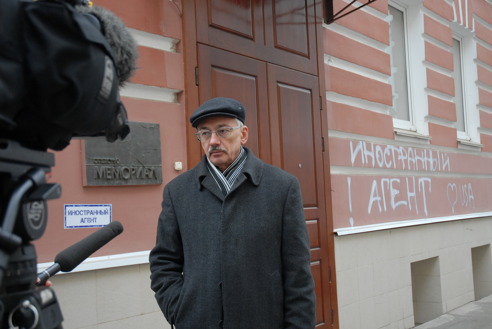 A man stands in front of a building with the words "foreign agent" painted on it.
